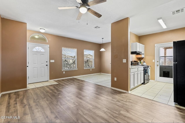 kitchen featuring gas range, hanging light fixtures, black refrigerator, light hardwood / wood-style floors, and white cabinets