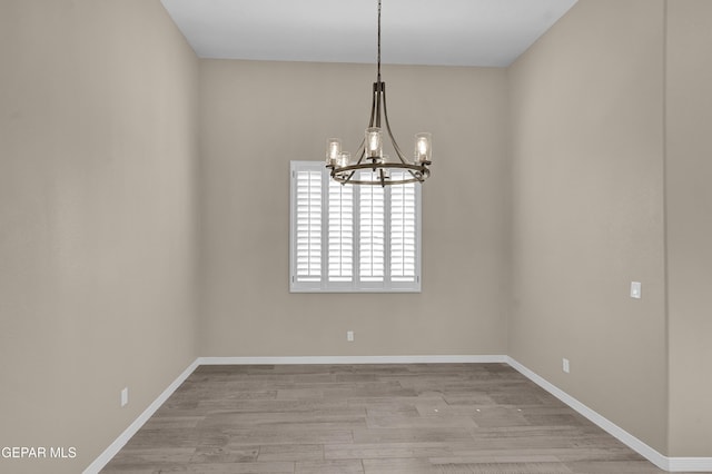 empty room featuring a notable chandelier and light hardwood / wood-style flooring