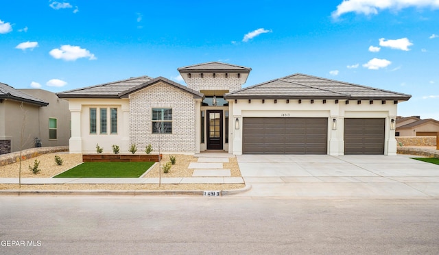 prairie-style home with brick siding, a tile roof, stucco siding, a garage, and driveway