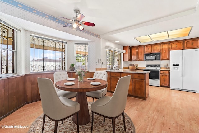 dining space featuring ceiling fan, wooden walls, sink, and light hardwood / wood-style flooring