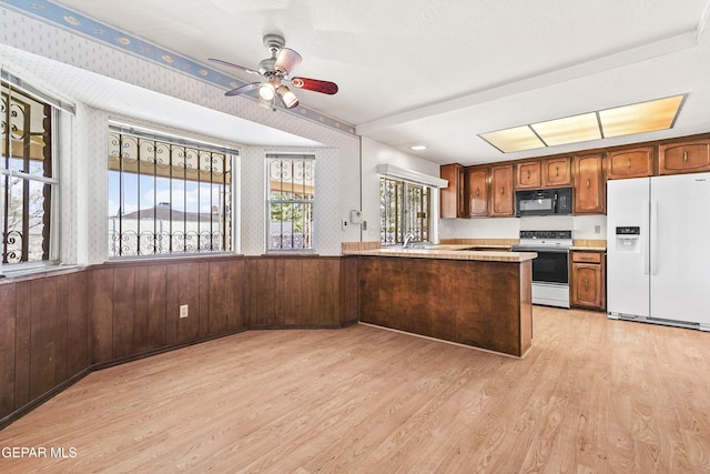 kitchen featuring white appliances, light hardwood / wood-style flooring, ceiling fan, kitchen peninsula, and wood walls