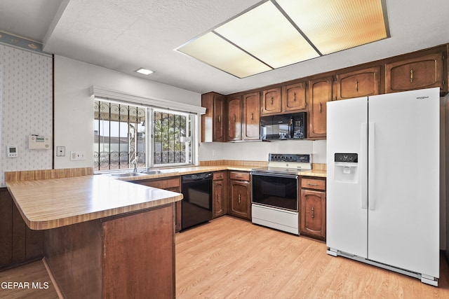 kitchen with light hardwood / wood-style flooring, black appliances, kitchen peninsula, and a textured ceiling