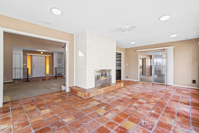 unfurnished living room with a brick fireplace, a textured ceiling, and ceiling fan