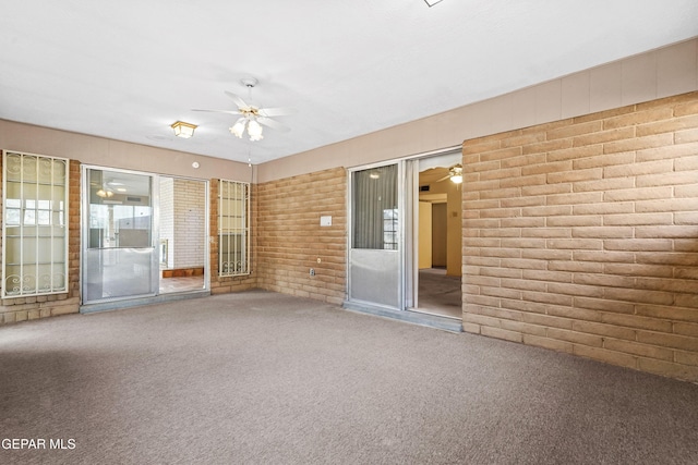 spare room featuring brick wall, carpet flooring, and ceiling fan