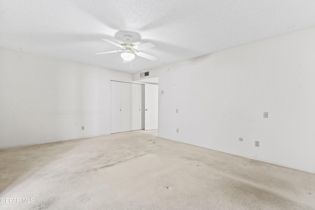 spare room featuring ceiling fan, light colored carpet, and a textured ceiling