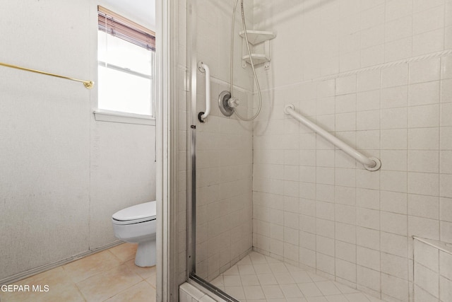 bathroom featuring toilet, a shower with shower door, and tile patterned flooring