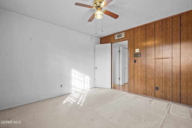 unfurnished room with wooden walls, light carpet, a textured ceiling, and ceiling fan