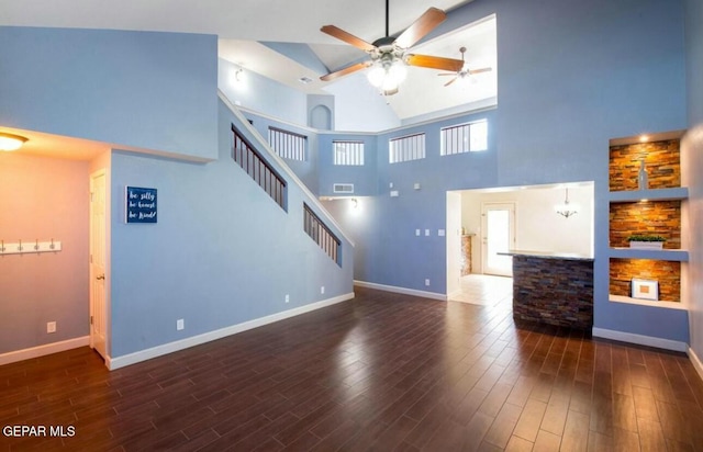 unfurnished living room with dark hardwood / wood-style floors, ceiling fan with notable chandelier, and a high ceiling