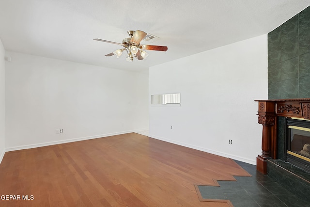 unfurnished living room featuring dark wood-style flooring, a large fireplace, baseboards, and ceiling fan