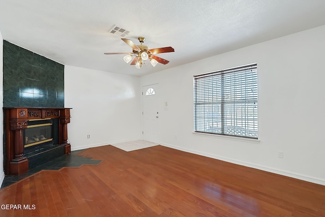 unfurnished living room with baseboards, visible vents, ceiling fan, wood finished floors, and a fireplace