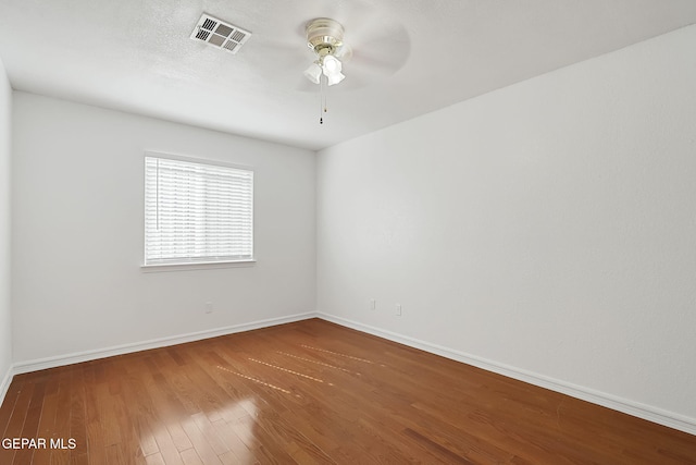 spare room with a ceiling fan, visible vents, baseboards, and wood finished floors