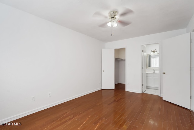 unfurnished bedroom with baseboards, ensuite bath, dark wood-style flooring, a spacious closet, and a closet