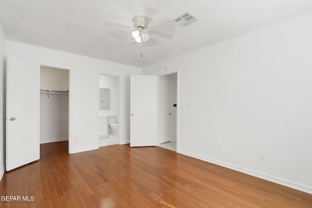 unfurnished bedroom with baseboards, visible vents, wood finished floors, a walk in closet, and a closet