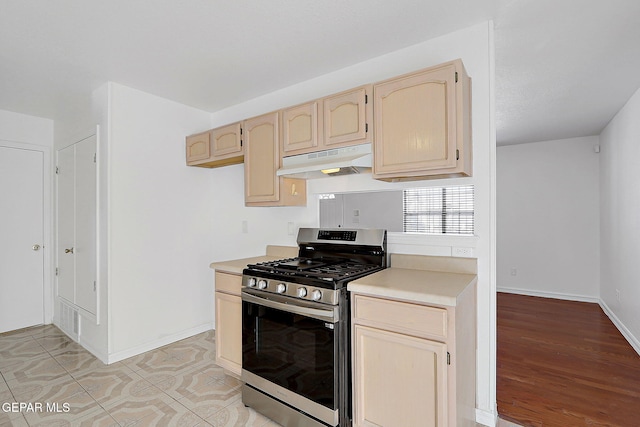 kitchen featuring light countertops, stainless steel gas range oven, light brown cabinets, and under cabinet range hood