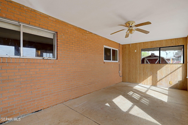 empty room featuring ceiling fan and brick wall