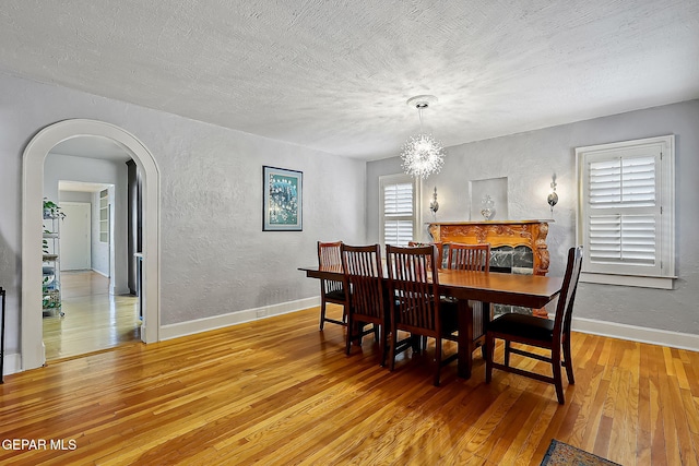 dining space with wood-type flooring, a textured ceiling, and a notable chandelier