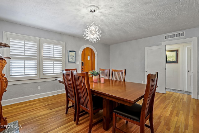 dining area with light hardwood / wood-style floors, a textured ceiling, and a notable chandelier