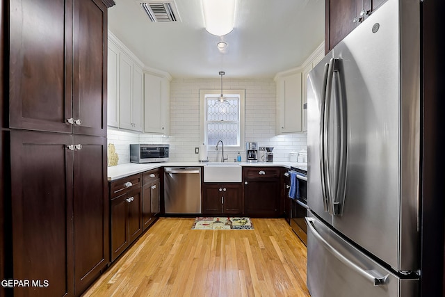 kitchen featuring sink, light hardwood / wood-style flooring, appliances with stainless steel finishes, pendant lighting, and backsplash