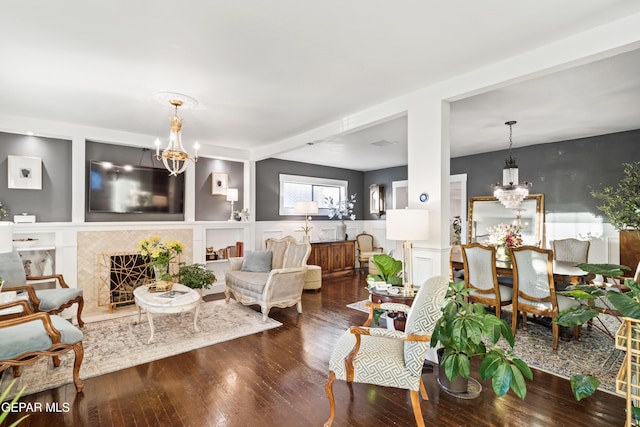 living room with hardwood / wood-style floors, built in shelves, a high end fireplace, and a chandelier