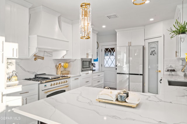 kitchen featuring premium range hood, white cabinets, white fridge, light stone counters, and gas range