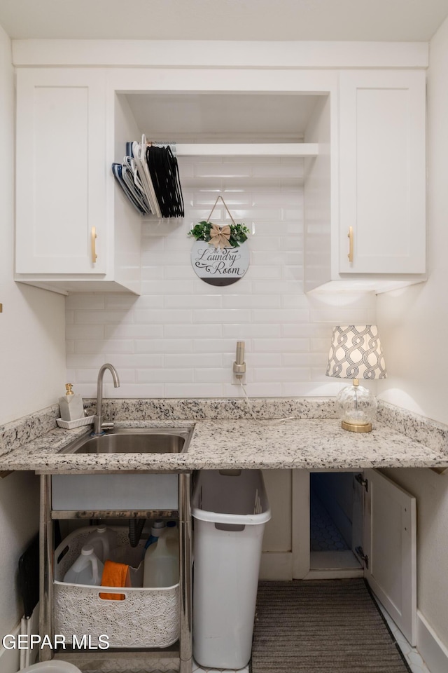 kitchen featuring white cabinetry, light stone countertops, sink, and backsplash