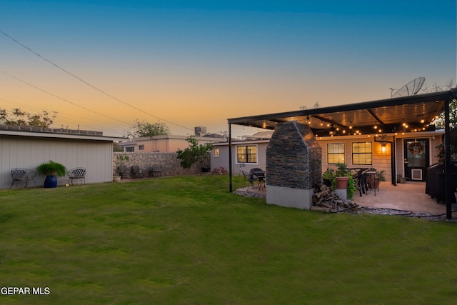 back house at dusk featuring a patio area and a lawn