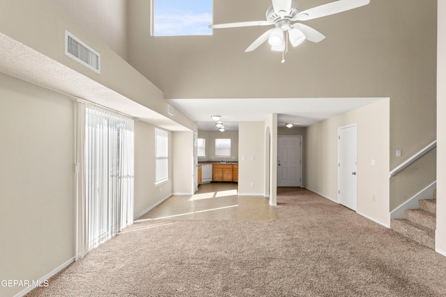 unfurnished living room featuring a high ceiling, light carpet, and ceiling fan