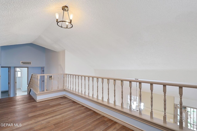 hall with an inviting chandelier, vaulted ceiling, hardwood / wood-style floors, and a textured ceiling