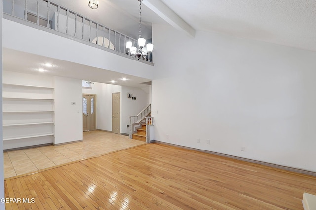 unfurnished living room featuring beam ceiling, high vaulted ceiling, light hardwood / wood-style floors, and a chandelier