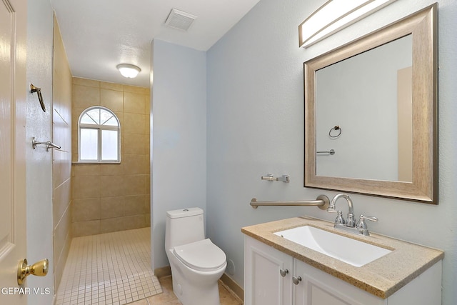 bathroom with a tile shower, vanity, and toilet