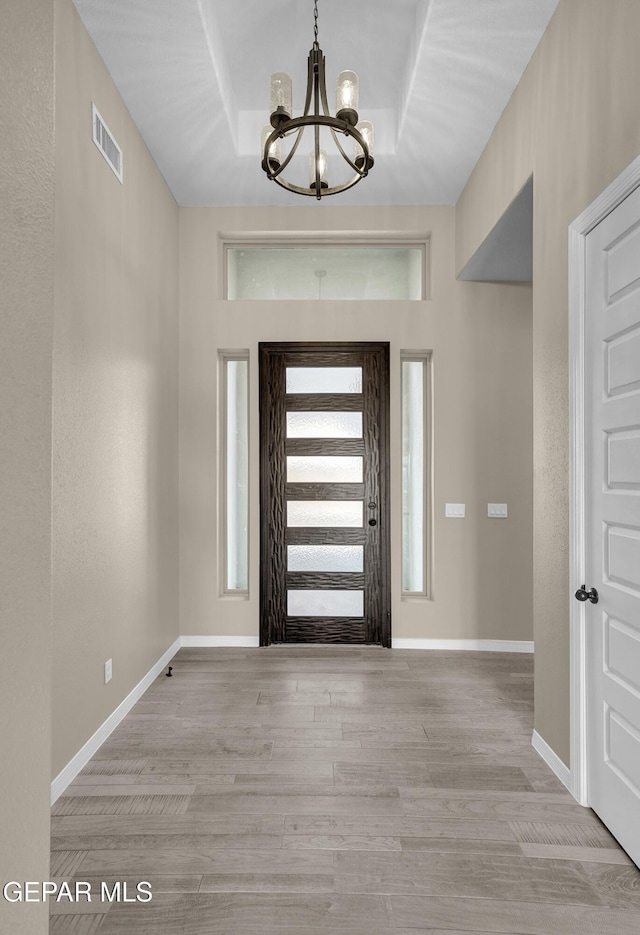 foyer entrance featuring light hardwood / wood-style flooring, a raised ceiling, and a chandelier