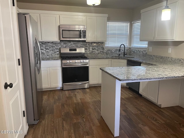 kitchen with light stone counters, pendant lighting, stainless steel appliances, kitchen peninsula, and white cabinets