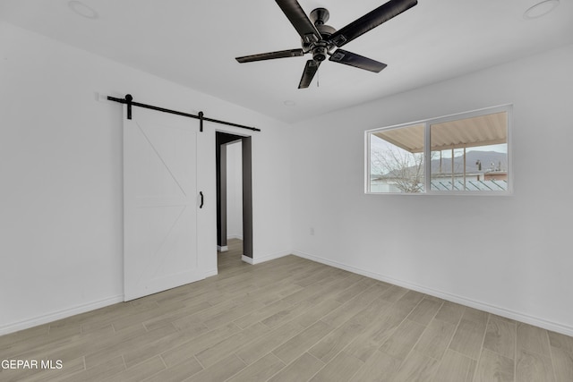 unfurnished bedroom featuring ceiling fan, a barn door, and light hardwood / wood-style flooring