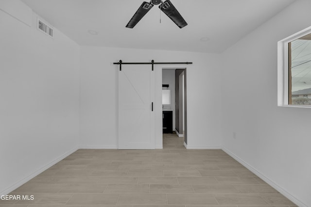 spare room featuring a barn door, light wood-type flooring, and ceiling fan