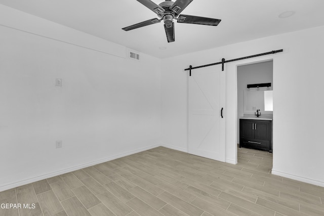 unfurnished bedroom featuring ceiling fan, a barn door, and ensuite bath