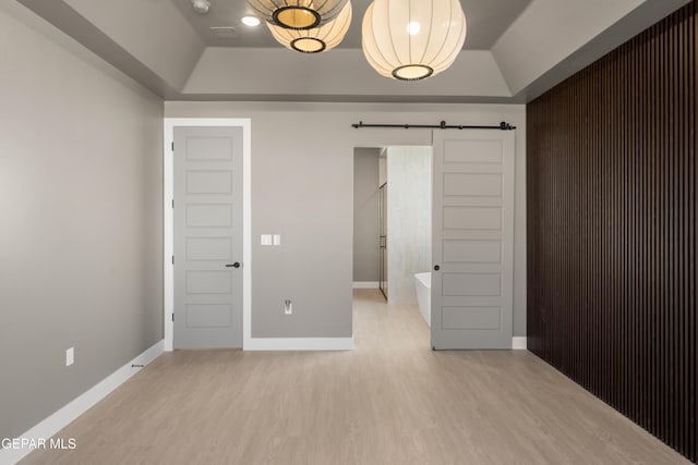 unfurnished bedroom with a barn door, a tray ceiling, and light hardwood / wood-style floors