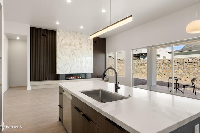 kitchen with sink, light stone counters, decorative light fixtures, a premium fireplace, and a kitchen island with sink