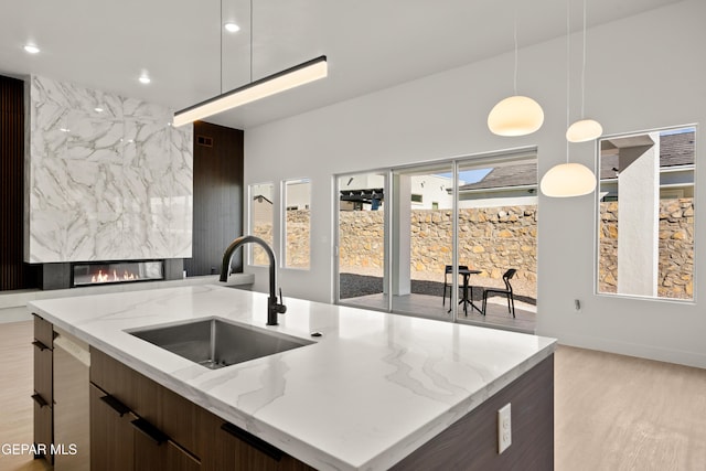 kitchen featuring pendant lighting, an island with sink, sink, light stone countertops, and light hardwood / wood-style flooring