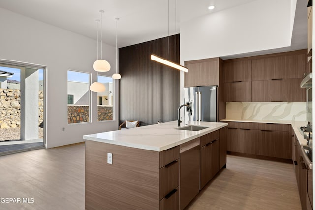 kitchen with pendant lighting, sink, light hardwood / wood-style flooring, appliances with stainless steel finishes, and a center island with sink