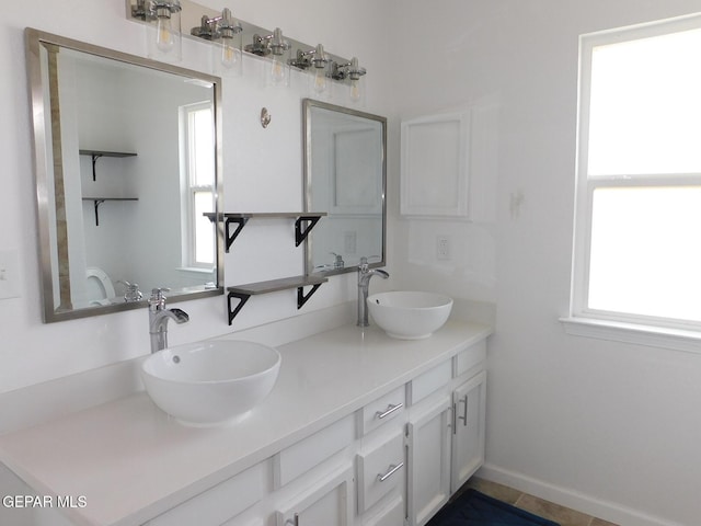 full bath featuring double vanity, a sink, and baseboards
