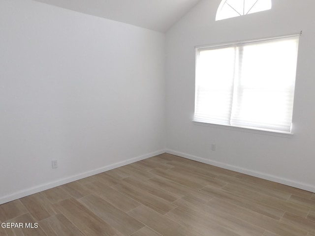 spare room featuring plenty of natural light, light wood finished floors, and lofted ceiling