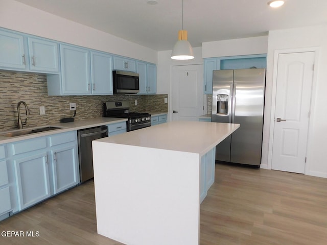 kitchen featuring blue cabinetry, tasteful backsplash, a sink, light wood finished floors, and stainless steel appliances