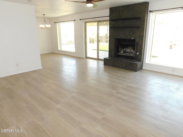 unfurnished living room with baseboards, light wood-style flooring, ceiling fan with notable chandelier, and a fireplace