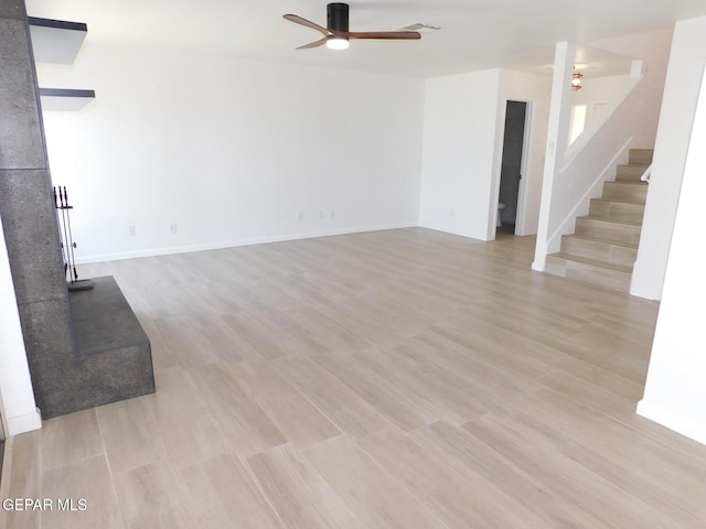 unfurnished living room with stairway, baseboards, a ceiling fan, and light wood-style flooring