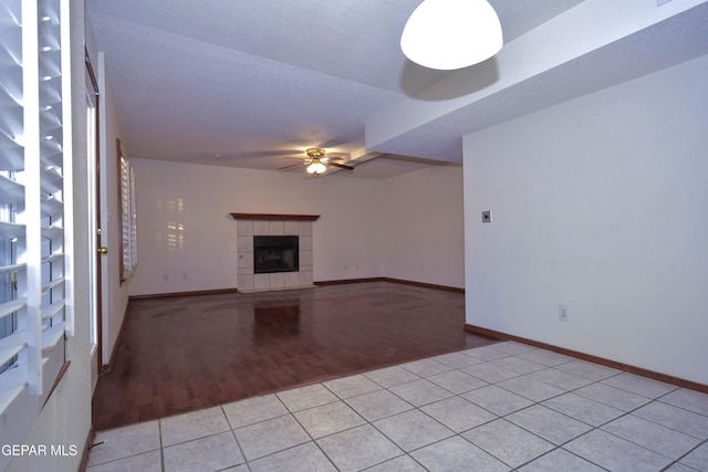 unfurnished living room with a textured ceiling, a tile fireplace, ceiling fan, and light tile patterned flooring