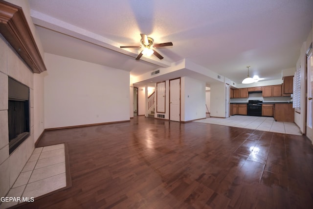 unfurnished living room with a textured ceiling, beamed ceiling, ceiling fan, a fireplace, and light hardwood / wood-style floors