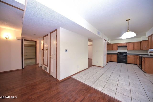 kitchen with decorative light fixtures, sink, black appliances, a textured ceiling, and light hardwood / wood-style flooring