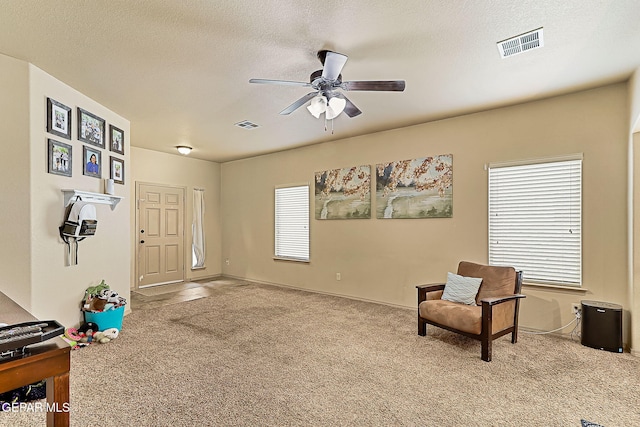 living area with ceiling fan, light carpet, and a textured ceiling