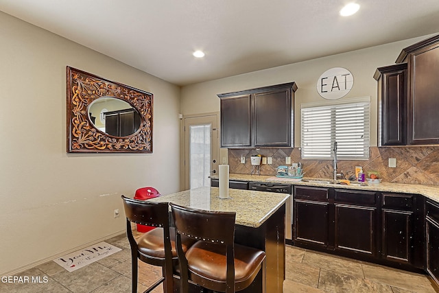 kitchen with sink, dark brown cabinets, a kitchen island, light stone countertops, and backsplash