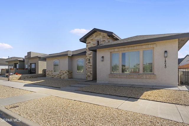 view of front of home featuring stone siding, fence, and stucco siding